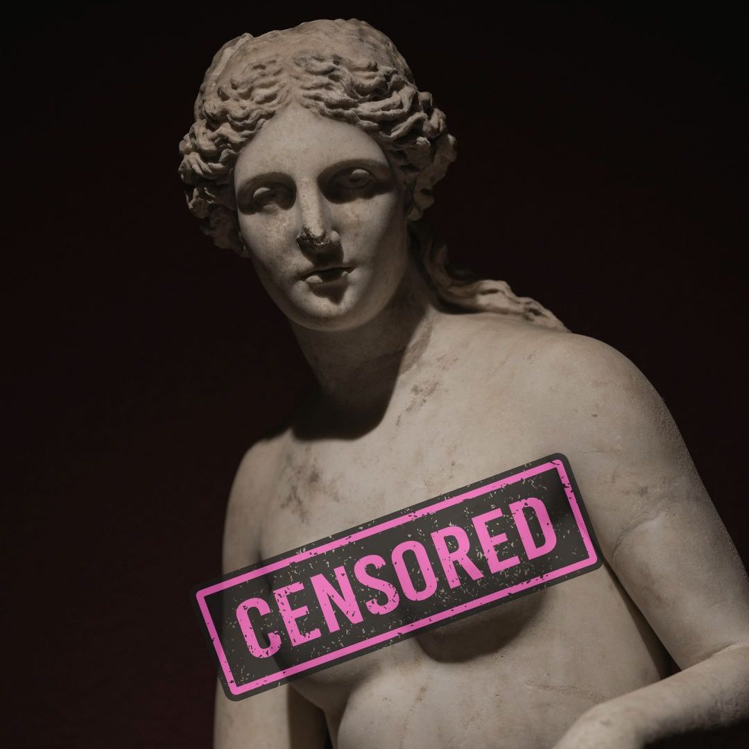 A close-up of a classical marble statue of a female figure with a censored label across its chest.